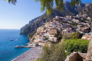 The sun shining on the beach and a colourful hillside of homes on the Amalfi Coast.