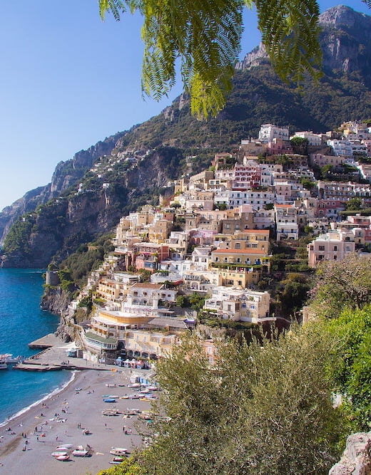 The sun shining on the beach and a colourful hillside of homes on the Amalfi Coast.