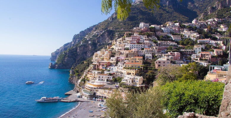 The sun shining on the beach and a colourful hillside of homes on the Amalfi Coast.