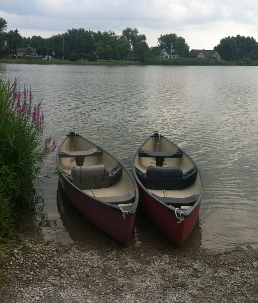 Two canoes on the water at the edge of a beach.