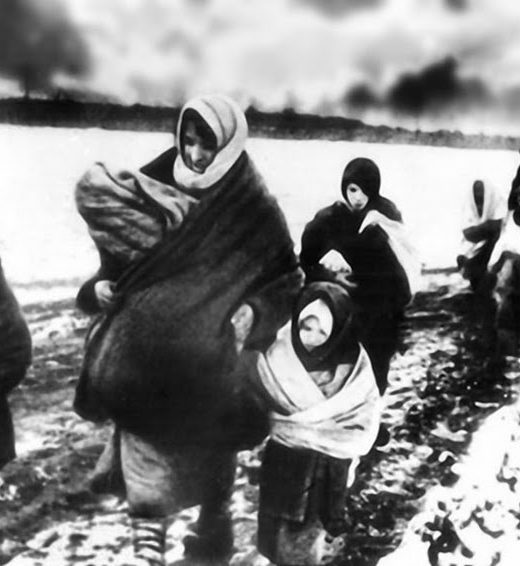 Women and children fleeing Ukraine on foot through the snow in World War II with only what they could carry, as building smoke in the background.
