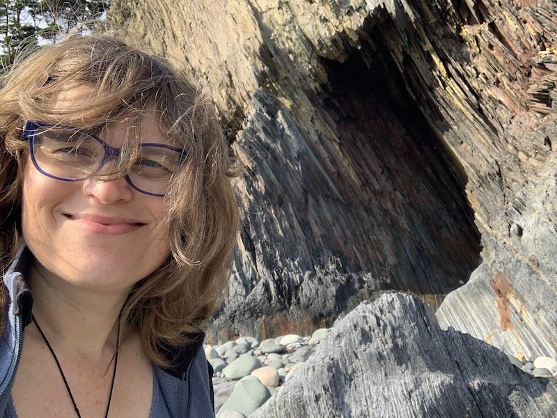 Smiling woman with a golden rock streaked cave behind her.