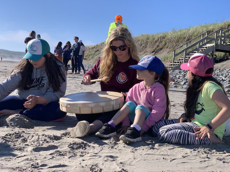 A woman surrounded by children testing out a drum on Mavillette Beach.