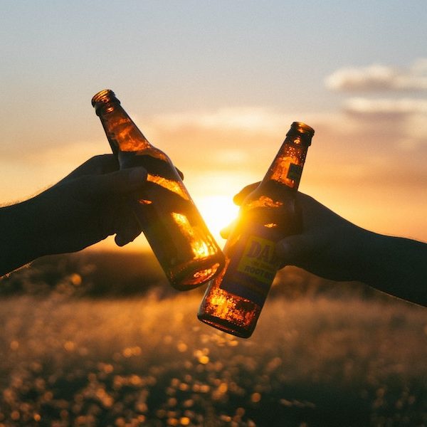 Clinking beer bottles at sunset.