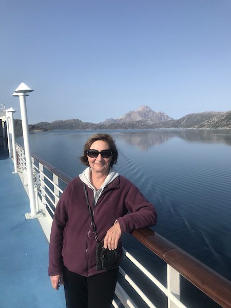Anne enjoying a walk around the deck of the Oceania Insignia with the fjords of Prince Christian Sound in the background.