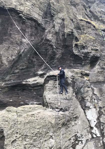 Ebbi Baldursson, holding a rope swing on a rock wall, as he demonstrates Sprangan.