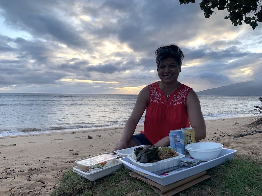 Beautiful woman smiling over a Da Kitchen Feast on the beach.