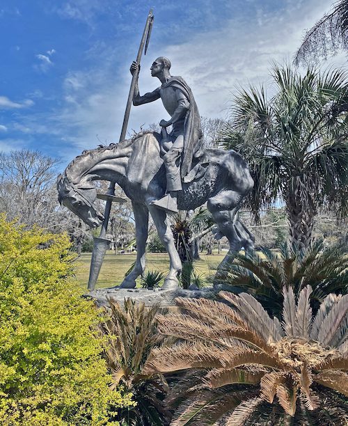 Sculpture of a man on a horse, wearing a cape and carrying a spear, in Brookgreen Gardens