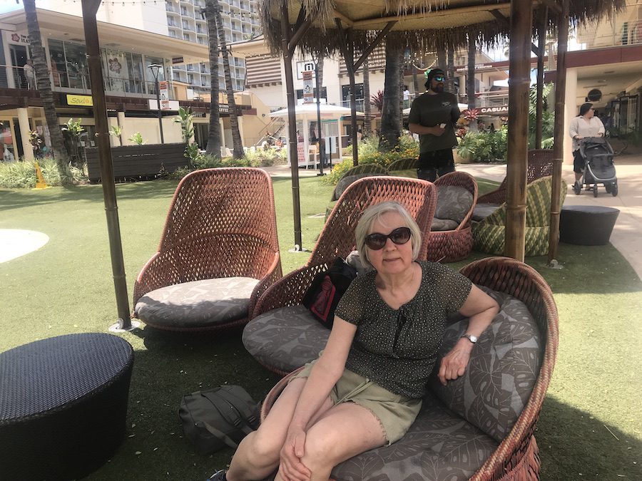 Vera enjoying a rest in a comfy chair in an outdoor shopping park for a bit of people watching, while waiting for a Maui bus.