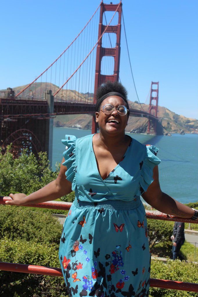 Pamela Pascal, wearing a blue dress and laughing at the Golden Gate Bridge