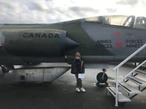 A young aviation lover poises into front of a Canadian Armed Forces Jet at the Canadian Museum of Flight