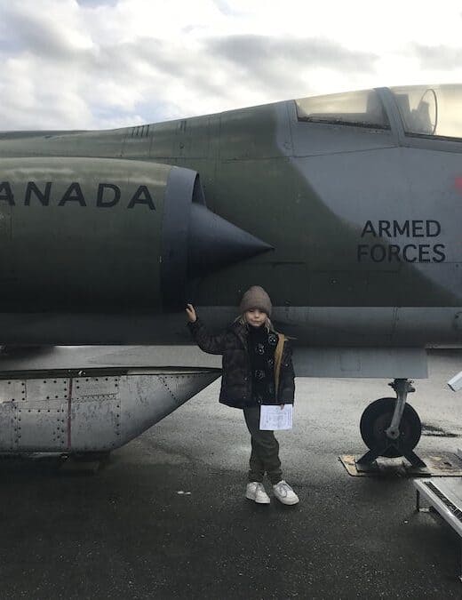 A young aviation lover poises into front of a Canadian Armed Forces Jet at the Canadian Museum of Flight