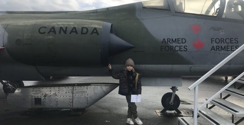 A young aviation lover poises into front of a Canadian Armed Forces Jet at the Canadian Museum of Flight