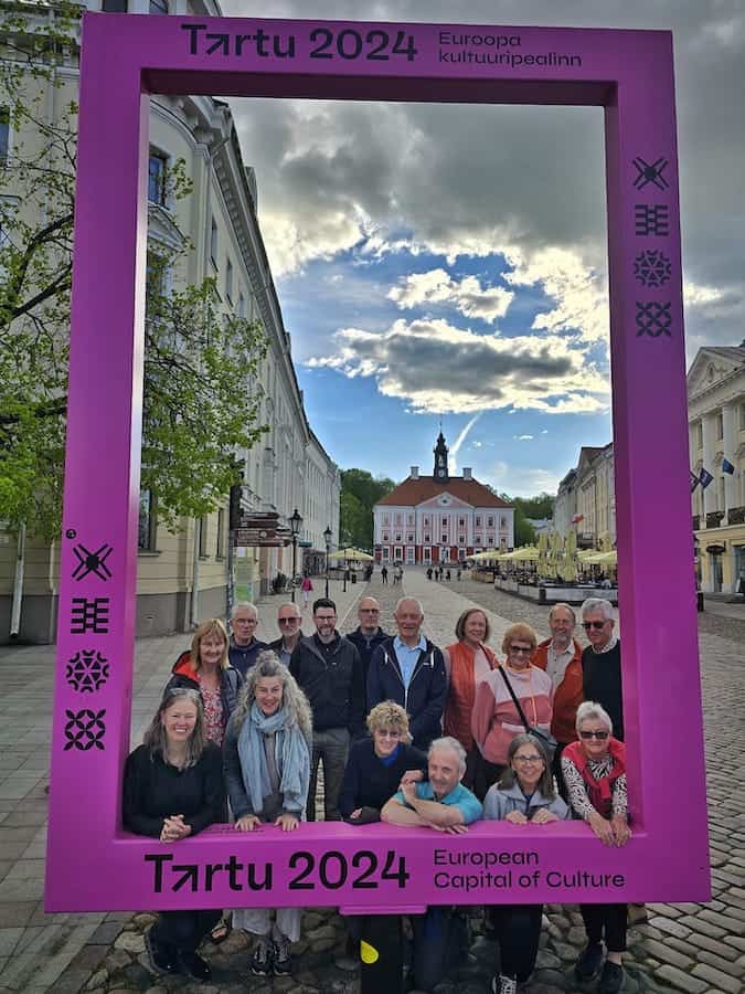 Our Exodus Adventure Travels group of 16 posing for a photo in a giant frame in Tartu, Estoni, towards the start of our journey cycling the Baltics together.