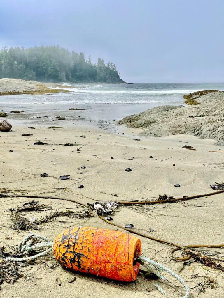 An orange buoy among washed up treasures on a beach along Cape Beale Trail.