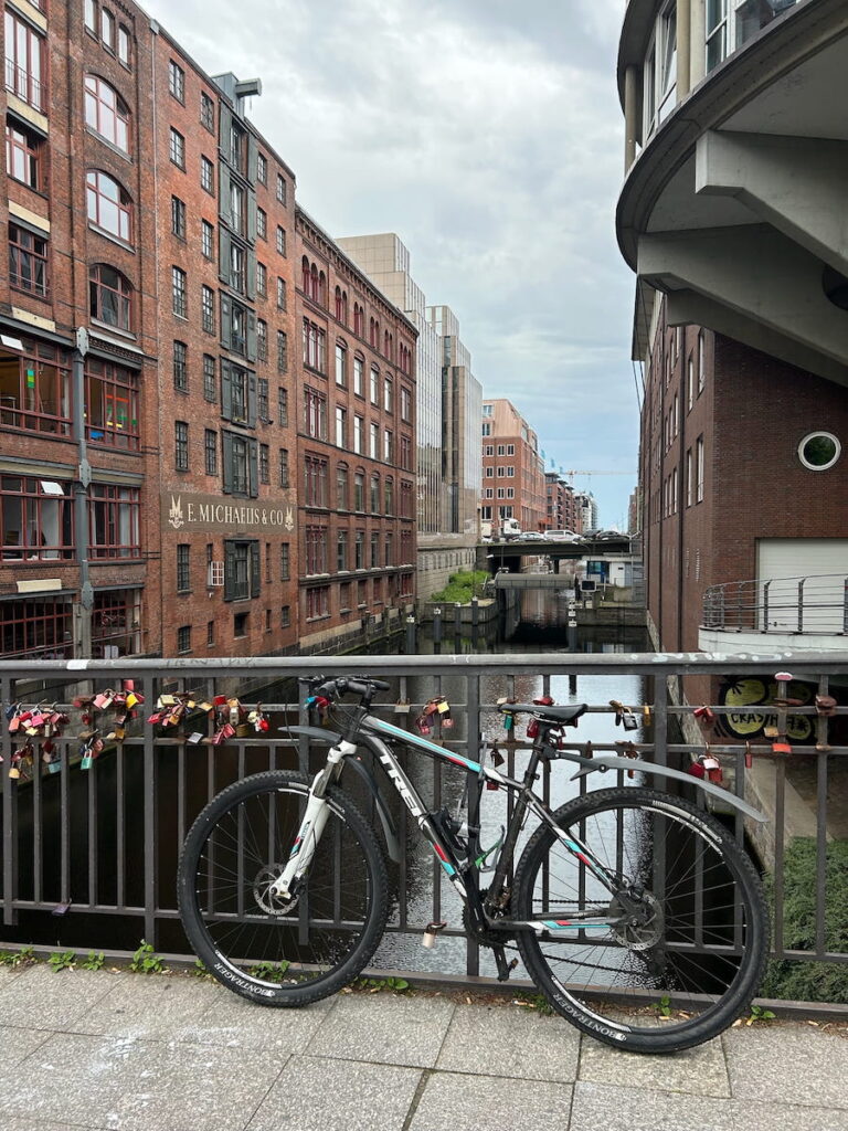 Romance on display in Hamburg Germany with love locks attached to a bridge over a canal bordered by red brick buildings. A bicycle leans against the bridge.