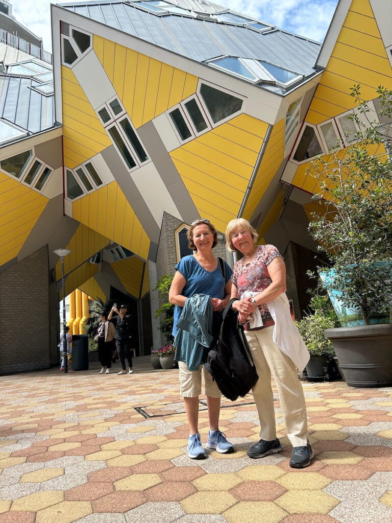 Writer Anne Webster and her sister Vera poise for a photo as Kijk-Kubus, Rotterdam's yellow Cube Homes, lean over them.