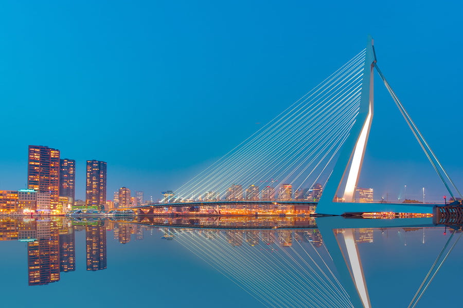 Erasmusbrug at night with the lights of the buildings on the bank reflecting on the water.