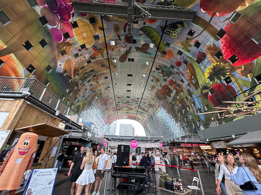 Inside Rotterdam's Markthal with its stunning ceiling featuring an 11,000 square meter painting called 'Horn of Plenty' and market stalls.