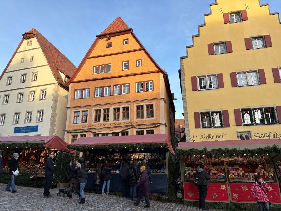 Stalls at the Rothenburg Ob Der Tauber Christmas Market under creme, orange and yellow buildings.