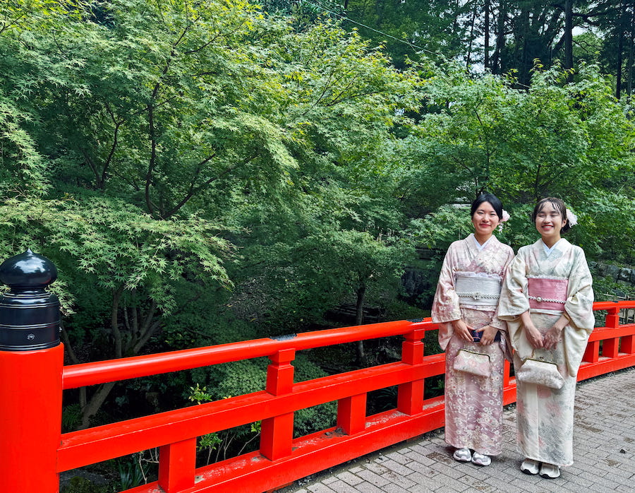 Two young girls in kimono pose on the red bridge at Fushimi Inari. Part of Japanese culture at shrines and temples in Japan.