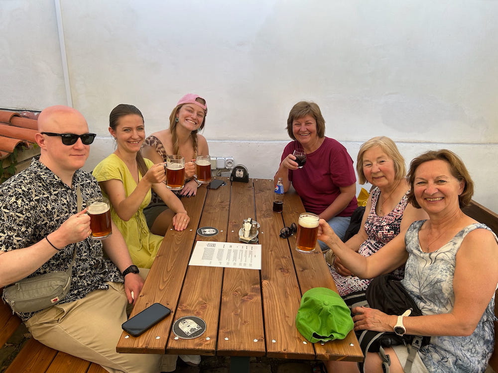 5 women and a man enjoying a brew around a long wooden table at St. Norbert Brewery, during four-days in Prague, Czechia.