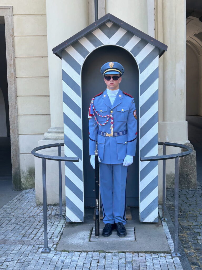 Prague Palace Guard standing on guard in a baby blue uniform in a blue and white striped guard house.
