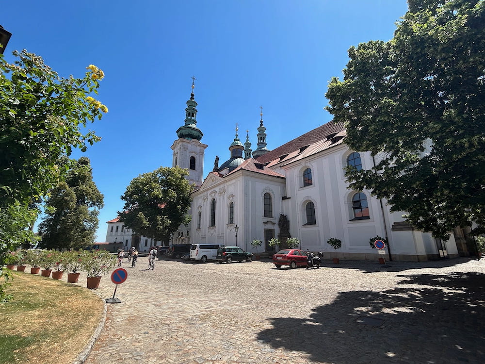 Cyclists bike past the beautiful buildings and grounds of Strahov Monastery in Prague, Czechia.