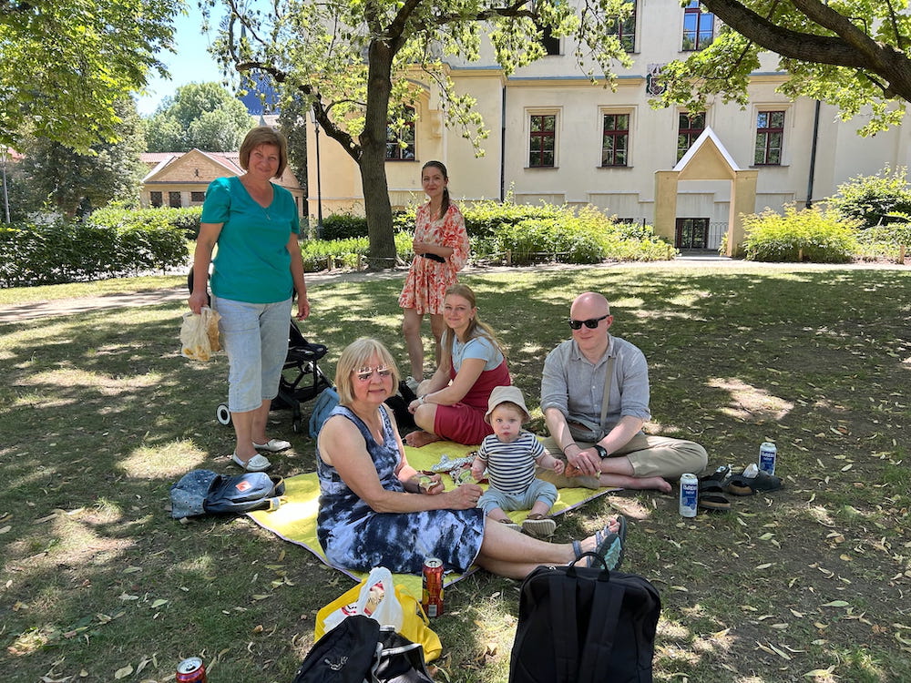 4 women, a man and a baby enjoying a picnic on the grounds of Vysehrad in Prague, Czechia on a sunny summer's day.