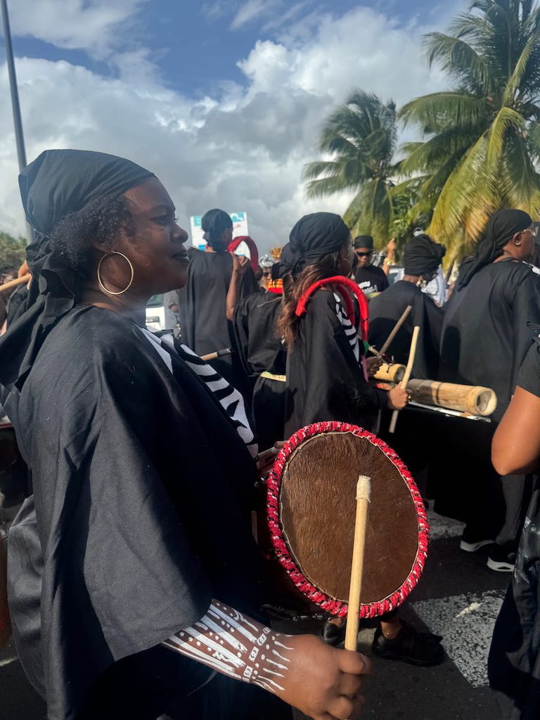 A band dressed in black with white skeleton arms, march and beat their drums at Martinique Carnival.
