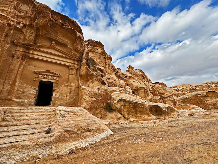 A cat poses on the steps of a building carved into the white rock of Siq Al-Barid (Little Petra).