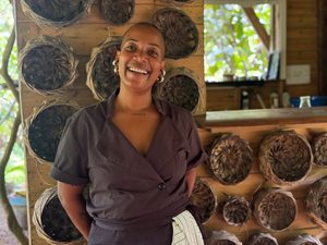 Cheffe Sterelle smiling at a Diner des Mornes, with a wall of hand woven bowls behind her.