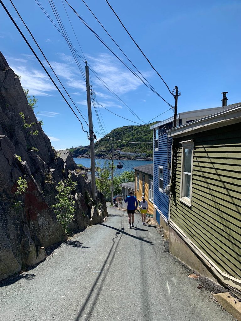 A couple walks between the hillside and colourfully painted homes, down to the St. John's harbour on a sunny Spring day.