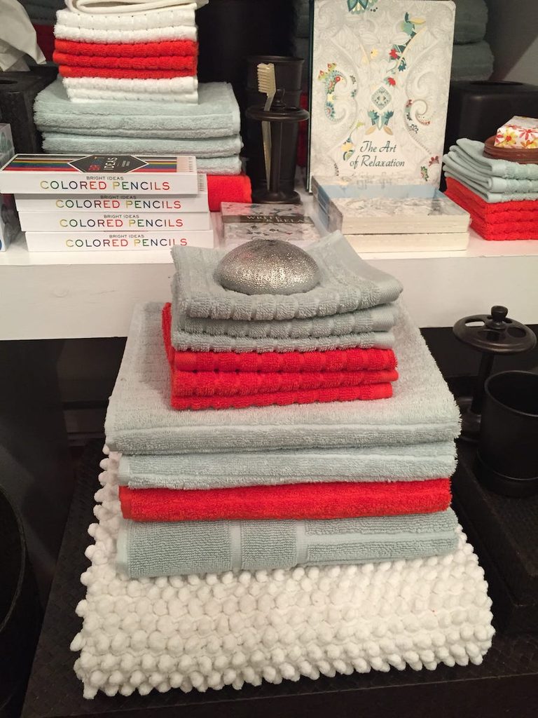 Beautifully folded bathroom towels in grey, red and cream topped with art deco sand dollar speak to calm in HOME on water st, along with The Art of Relaxation colouring book and colouring pencils.