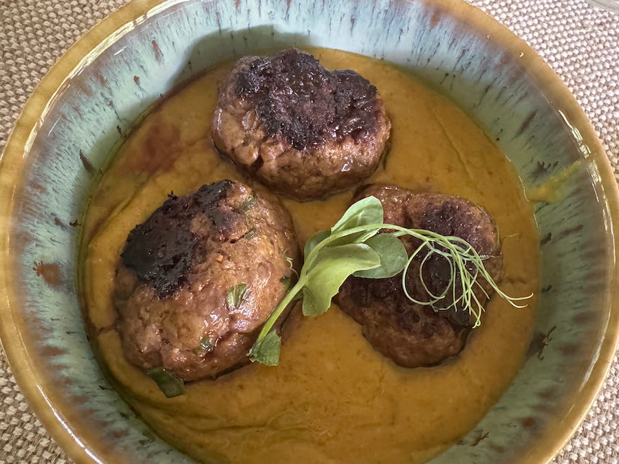 3 beef meatballs in a sauce in a pottery bowl - a Chef Sterelle creation.
