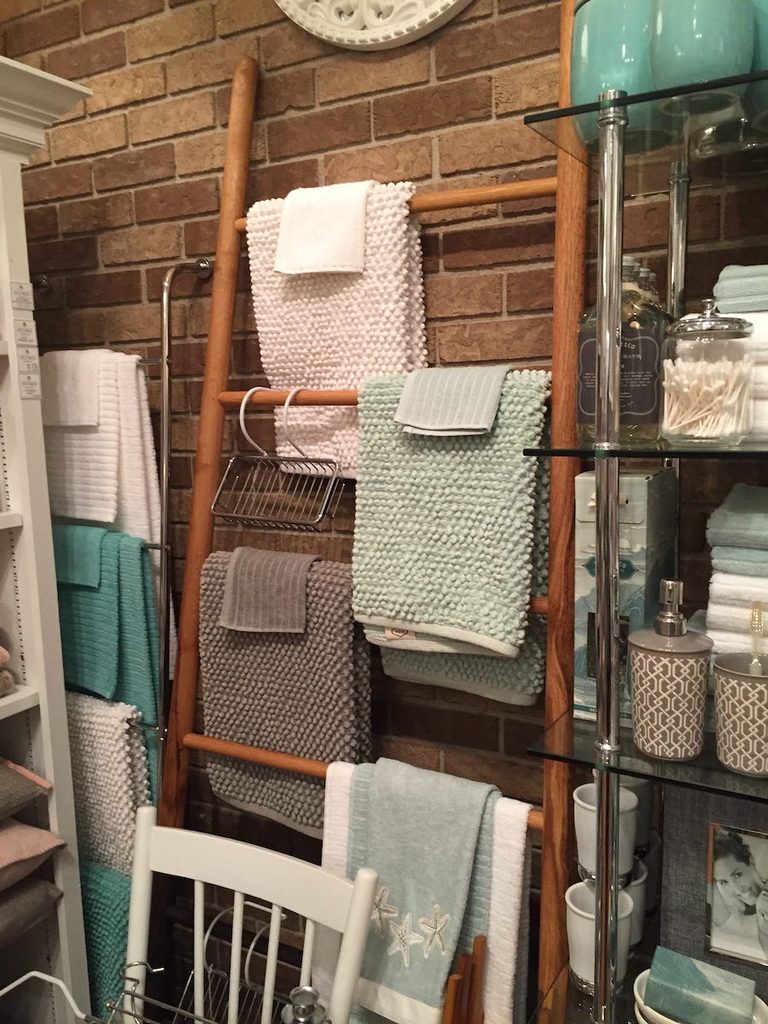 Neatly folded fluffy towels on a wooden wall wrack, leaning against a red brick wall in HOME on water st.